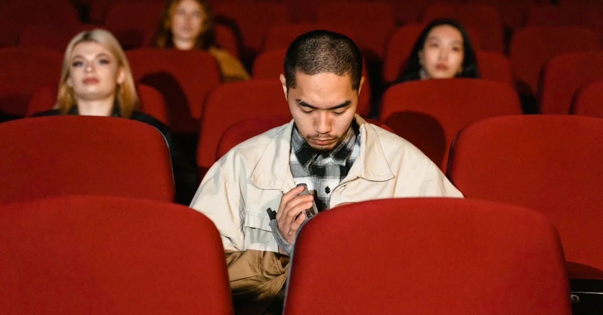 Un groupe divers assis dans une salle de cinéma, regardant sérieusement.