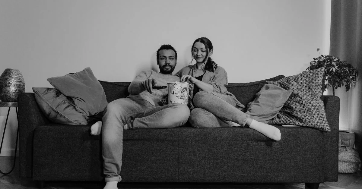 Un couple se détendant sur un canapé, partageant du pop-corn et profitant de l'instant dans un cadre chaleureux.