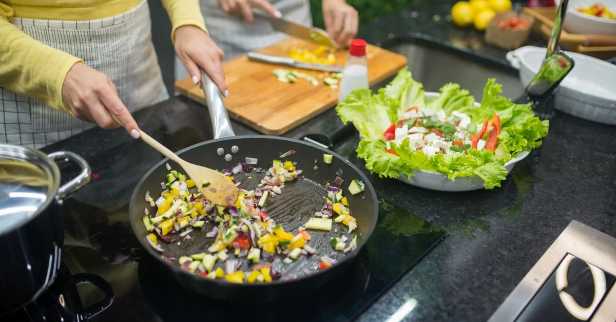 Deux adultes cuisinent des légumes frais sur une cuisinière, préparant un repas sain dans une cuisine moderne.
