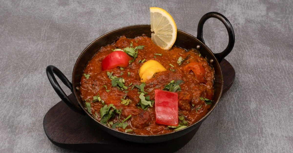 Un curry indien coloré, garni de poivrons et d'une tranche de citron, dans un plat traditionnel.