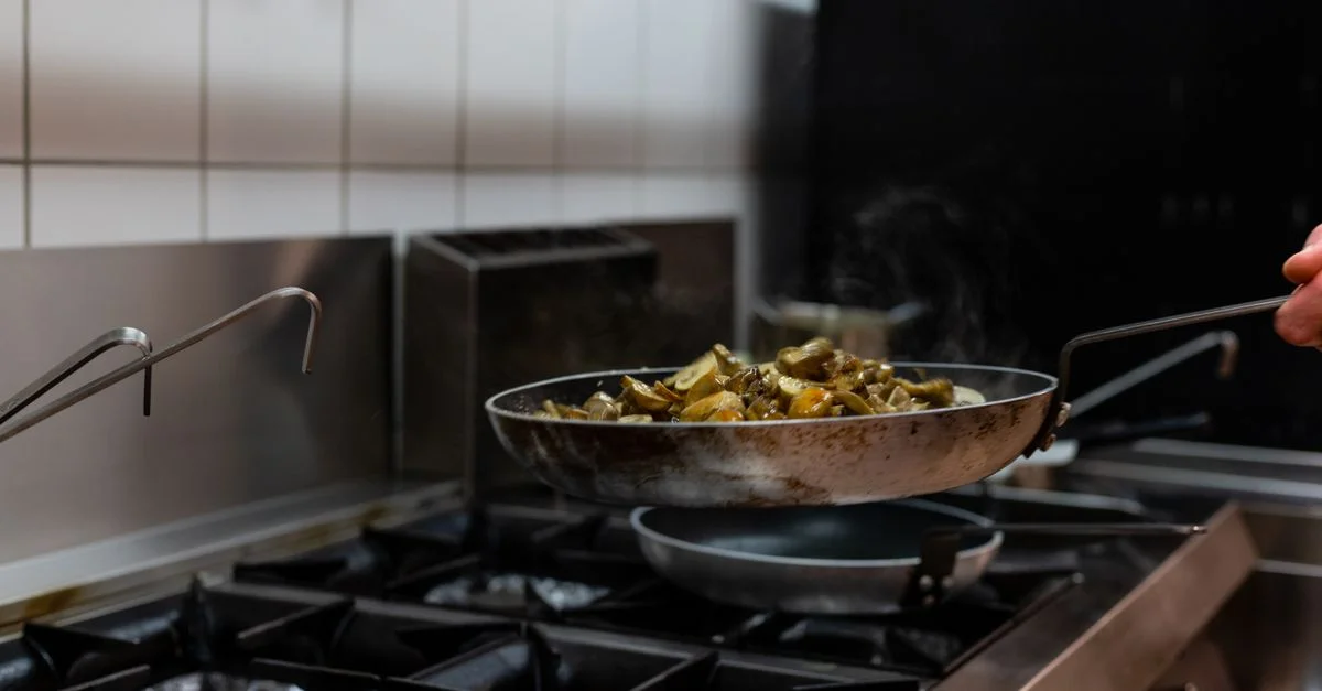 Des champignons grésillant en train d'être sautés dans une poêle dans un cadre de cuisine professionnelle, mettant en valeur la préparation culinaire.